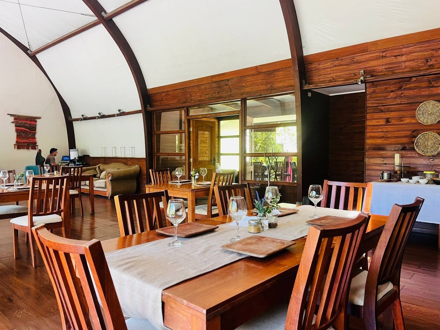 La mesa larga del comedor puesta, con copas de vino y platos, bajo el techo abovedado del salón